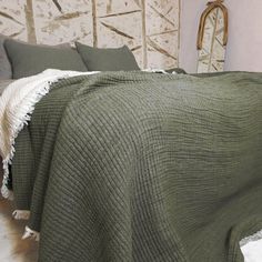 a bed with a green blanket on top of it next to pillows and a mirror