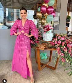 a woman in a pink dress standing next to a table with flowers and balloons on it