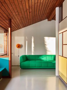 a green couch sitting in the middle of a living room next to a wooden ceiling