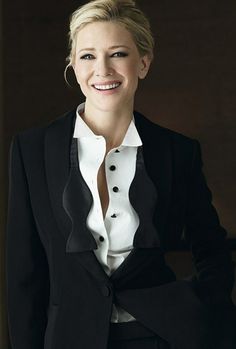 a woman in a black suit and white shirt smiles at the camera with her hands on her hips