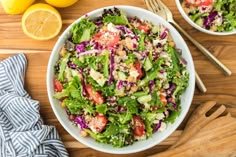 two bowls filled with salad on top of a wooden table next to sliced lemons