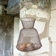 a wire basket hanging from the side of a wall with eggs in it and other items inside