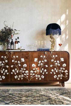 a sideboard with flowers painted on it in front of a lamp and vases