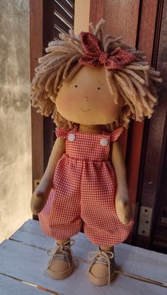 a doll with blonde hair wearing a red and white checkered dress sitting in front of a wooden door