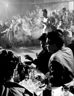 an old black and white photo of people sitting at a table in front of a crowd