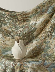 a white vase sitting on top of a bed next to a wallpaper covered in trees