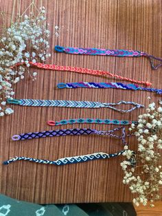 several different types of bracelets sitting on top of a wooden table next to flowers