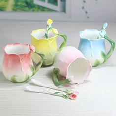 four different colored vases with spoons on a table next to eachother