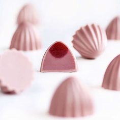 some pink chocolates on a white surface with one red piece in the middle and several other