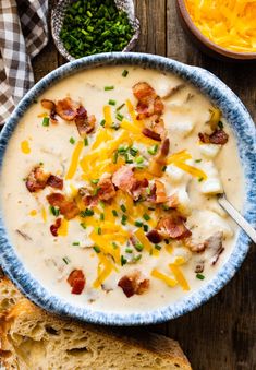 a bowl of potato soup with bacon and cheese in it next to bread on the side