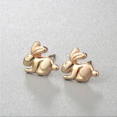 two gold colored rabbit shaped earrings sitting on top of a silver surface with white background