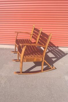 two wooden rocking chairs sitting in front of a red garage door on the side of a building