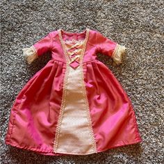 a doll is laying on the floor wearing a pink and white dress with gold trim