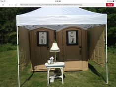 two portable toilets are set up in the grass near a table with a lamp on it