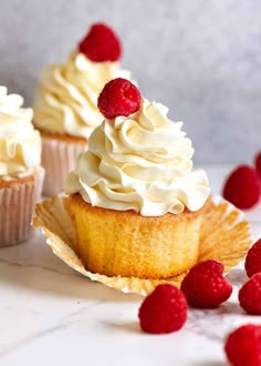 three cupcakes with white frosting and raspberries on the top one