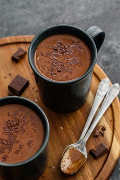 two cups of chocolate on a wooden tray with spoons