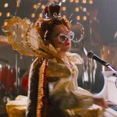 a woman wearing glasses and a headdress sitting in front of a piano with a microphone