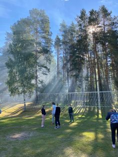 several people are standing in the grass near trees and a net on a sunny day