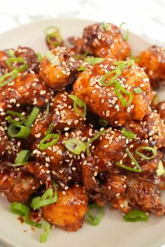 a white plate topped with chicken covered in sesame seeds and garnished with green onions