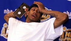 a young man holding up a video game controller to his head while standing in front of a blue wall