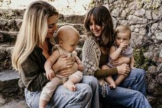 three women and two babys sitting on some steps smiling at each other with their arms around one another