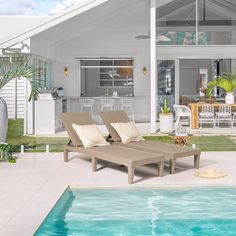 two lounge chairs sitting next to a swimming pool in front of a white house with palm trees