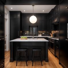 a large kitchen with black cabinets and white counter tops, two stools at the island