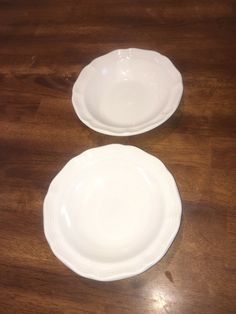 two empty white plates sitting on top of a wooden table next to each other,