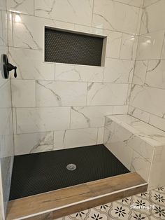 a white tiled bathroom with black and white floor tiles on the shower wall, along with a wooden bench