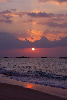 the sun is setting over the ocean with clouds in the sky and water on the beach