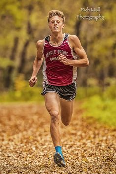 a man is running in the woods with leaves on the ground and trees behind him