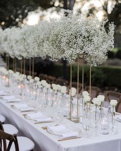 a long table with white flowers in vases and place settings on the tables is set for an event