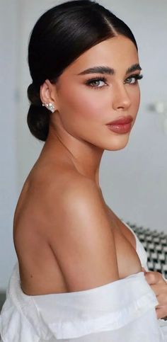 a woman with dark hair wearing a white dress and diamond earrings, looking off to the side