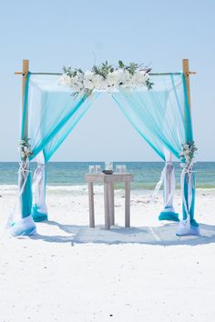 an outdoor wedding setup on the beach with blue drapes and white flowers in vases