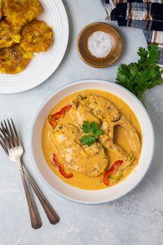 a white bowl filled with yellow curry next to some silverware and other food items