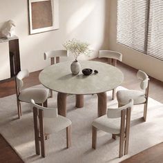 a round table with four chairs and a vase on it in front of a window