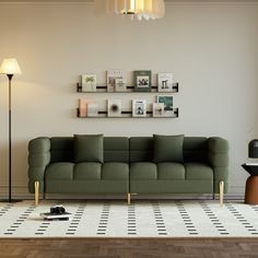 a green couch sitting on top of a wooden floor next to a lamp and pictures