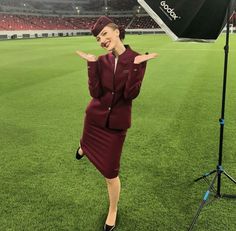 a woman in a red suit and hat standing next to an umbrella on a field