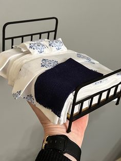 a hand is holding a bed with white and blue blankets on it, while another hand holds a black metal bed frame