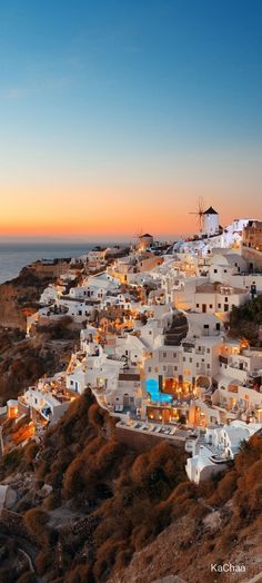 an aerial view of white buildings on the cliff by the ocean at sunset, with windmills in the distance