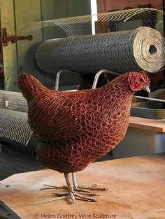 a chicken standing on top of a wooden table next to two rolls of yarn in the background