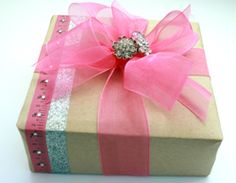 a wrapped present box with pink ribbon and jeweled bow on it's side