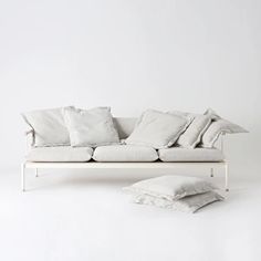 a white couch sitting next to pillows on top of each other in front of a white wall