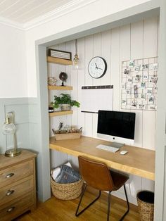 a desk with a computer on it in front of a wall mounted clock and other items