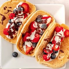 three pancakes with strawberries, blueberries and whip cream on them sitting on a white plate