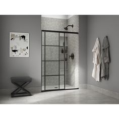 a walk in shower sitting next to a white tiled wall and grey walls with towels hanging on the rack