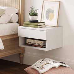 a white nightstand with books on it next to a bed and a potted plant