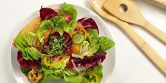 a white plate topped with lettuce and mixed veggies next to a wooden utensil