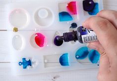 a person holding a bottle of paint next to some crafting supplies on a table