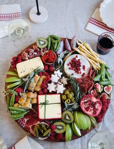 a platter filled with cheese, fruit and crackers next to wine glasses on a table